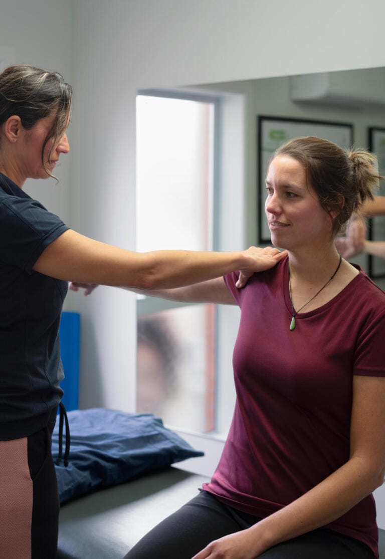 Physiotherapist assessing woman's shoulder in clinic